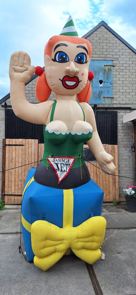 Grote opblaasbare figuur van een vrouw met rode haren en groene kleding, met een feestelijke uitstraling.