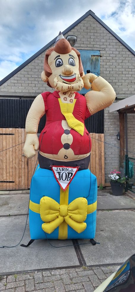 Groot opblaasfiguur van een man met een geel-shirt en een cadeau met een strik.